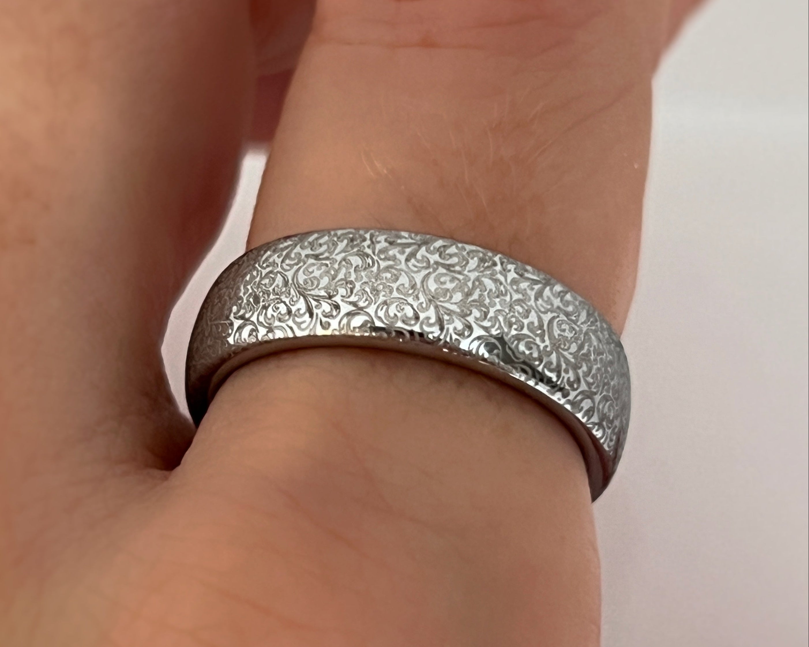 Silver ring with textured design on a finger against a white background