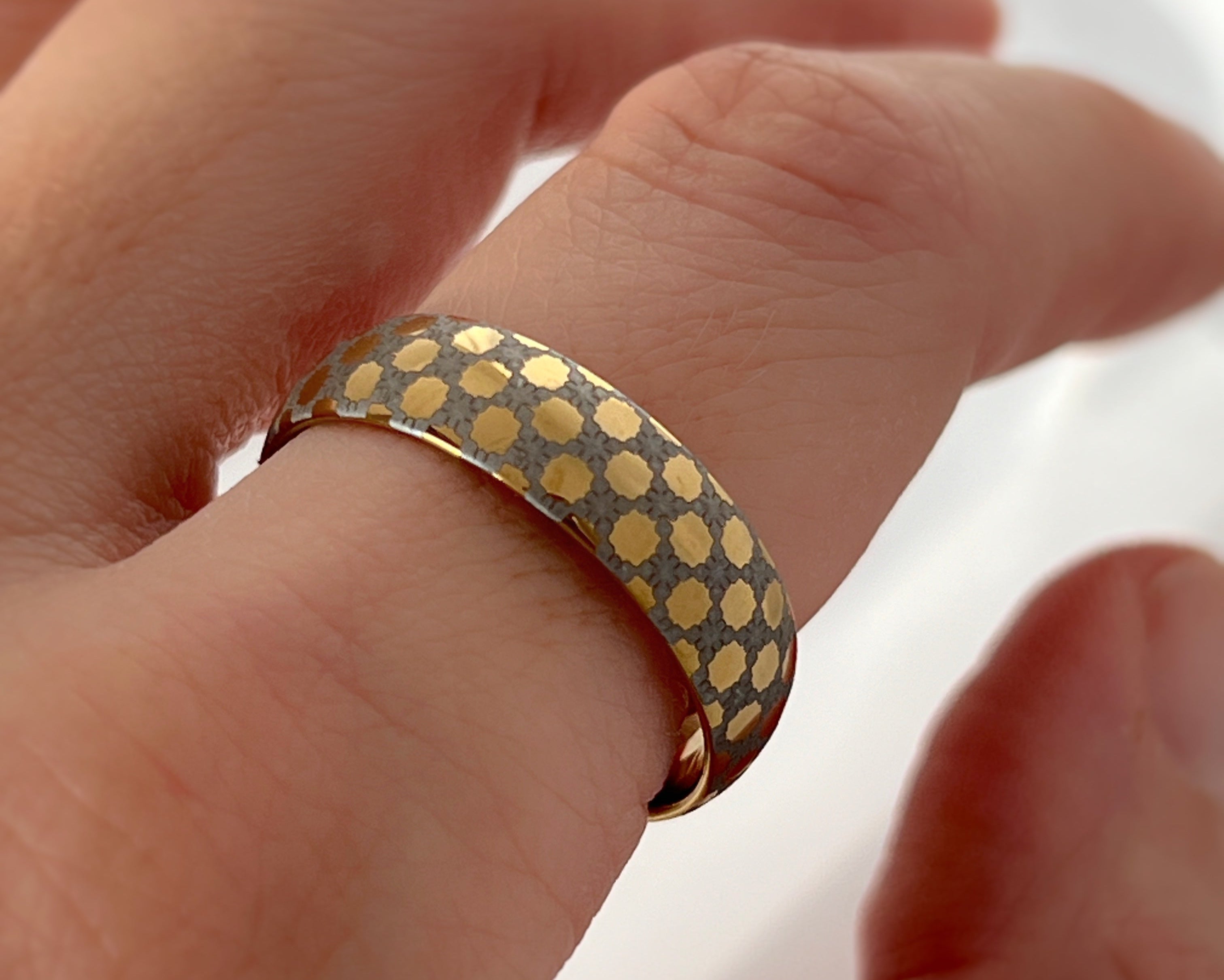 Hand wearing a gold polka dot ring on a blurred background