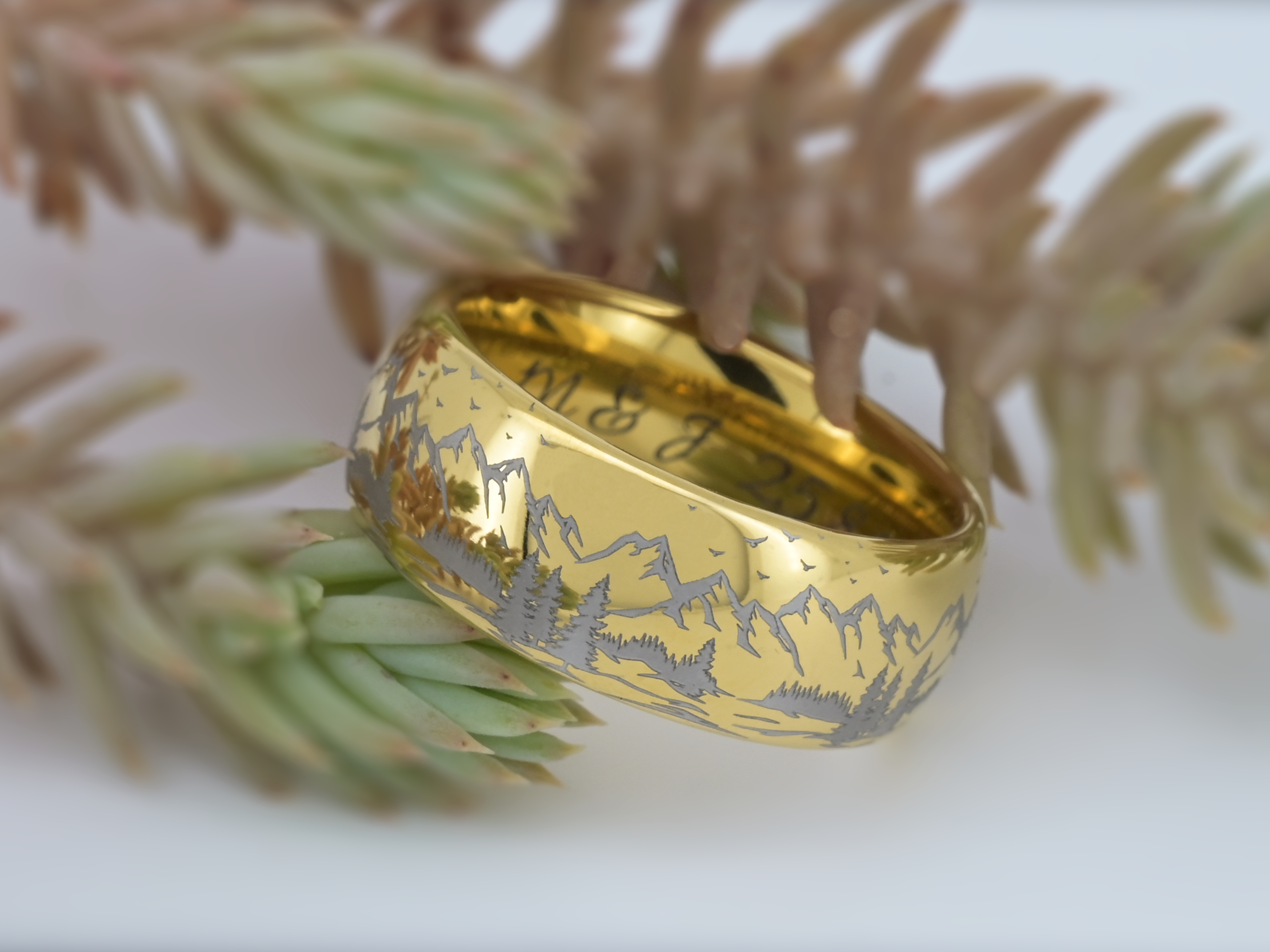 Close-up of a gold tungsten ring with detailed mountain engraving and silver-grey landscape pattern.