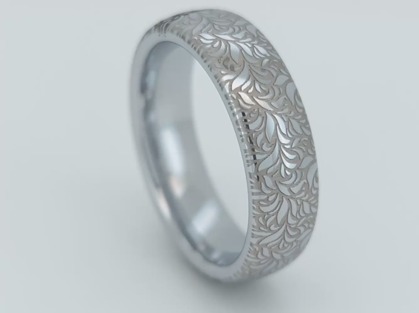 A video of elegant white gold tungsten displayed on the white background. The ring has intricate silver floral engraving, featuring a polished shiny finish and delicate patterns. Durable and stylish, this engraved tungsten wedding or engagement band for her or him