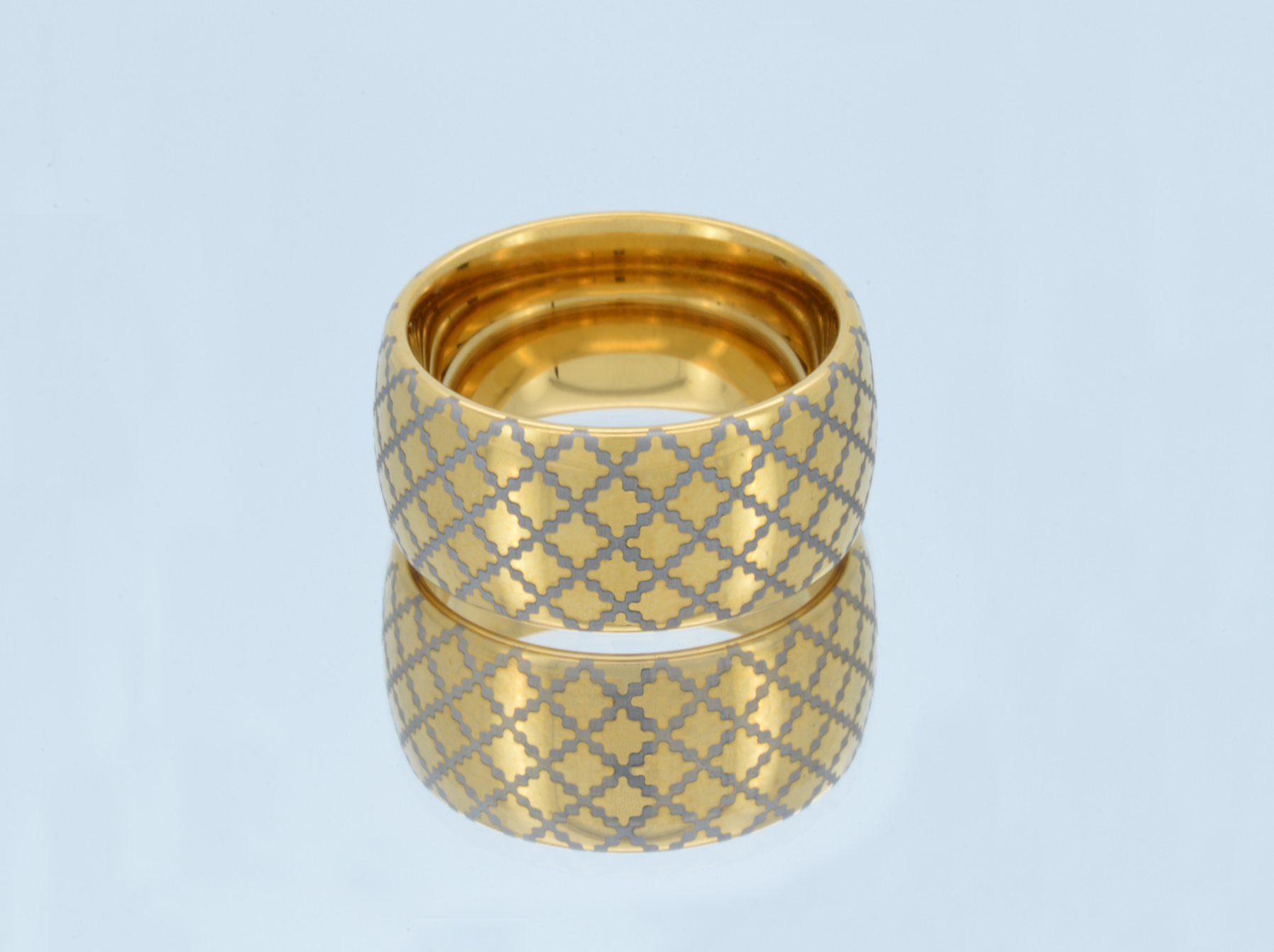 Gold tungsten ring with a quilted pattern, placed on a reflective surface, showcasing the detailed design.