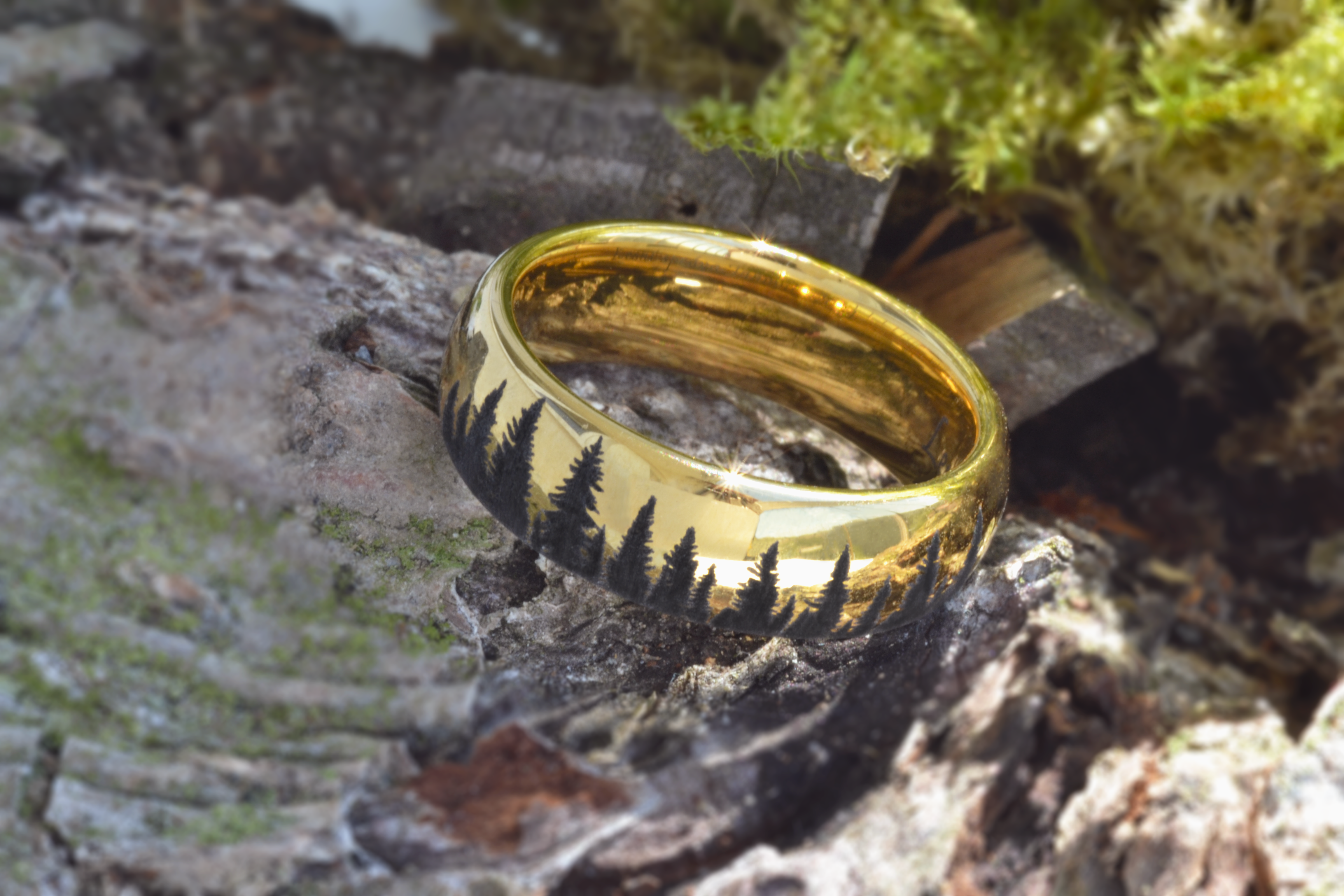 Gold tungsten ring with an engraved silhouette of an evergreen forest, placed on a piece of bark with moss, showcasing the nature-inspired design