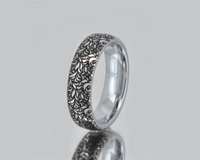 Engraved tungsten ring featuring an intricate black leaf and botanical pattern on a polished silver band. Nature inspired wedding band with elegant detailed design.