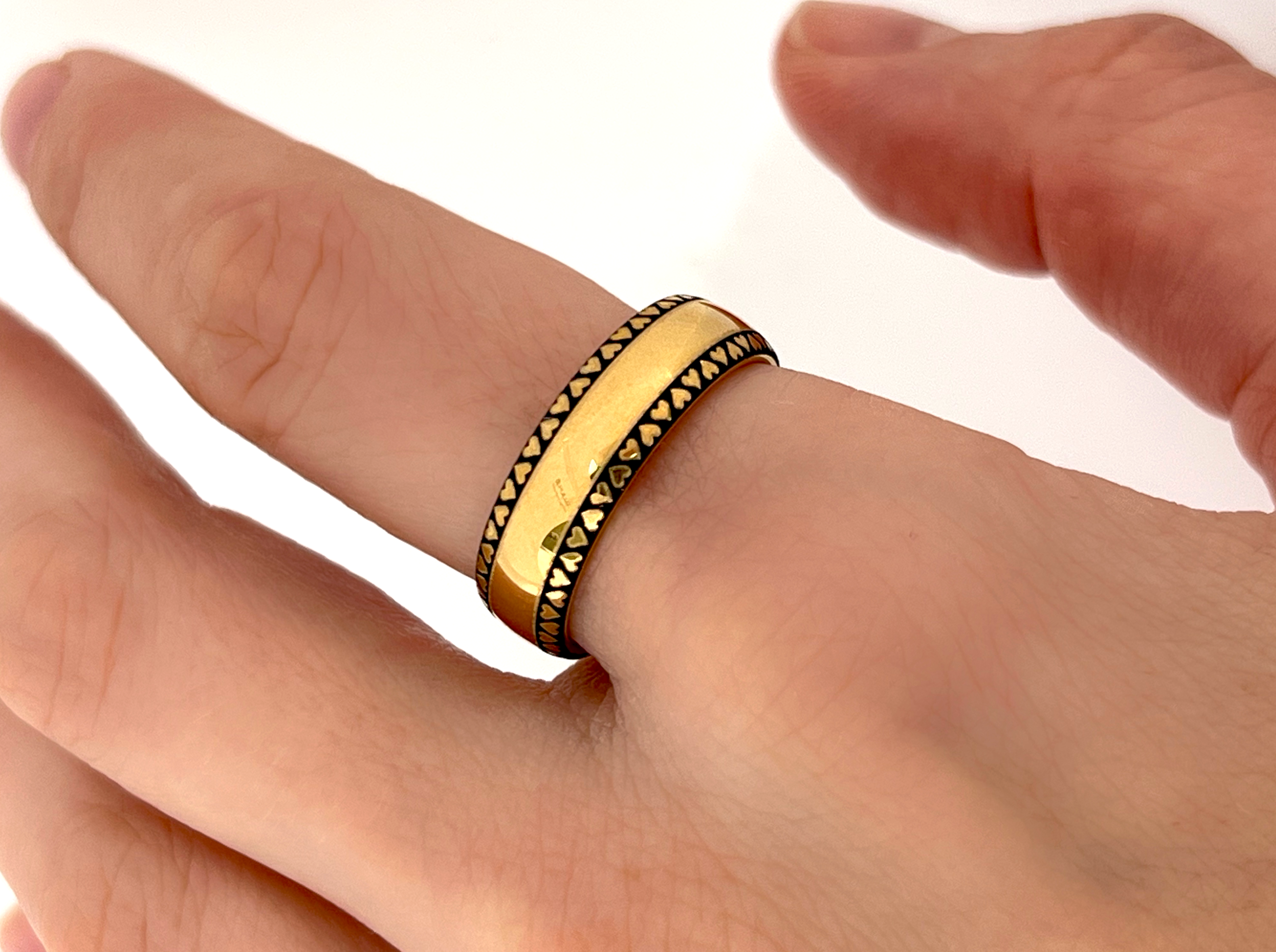 Close-up of the 'Eternal Love Band' on a finger, showcasing a gold finish with a continuous pattern of black hearts around its circumference.