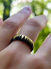 Gold tungsten ring with an engraved silhouette of an evergreen forest, worn on a finger, showcasing the detailed forest design.