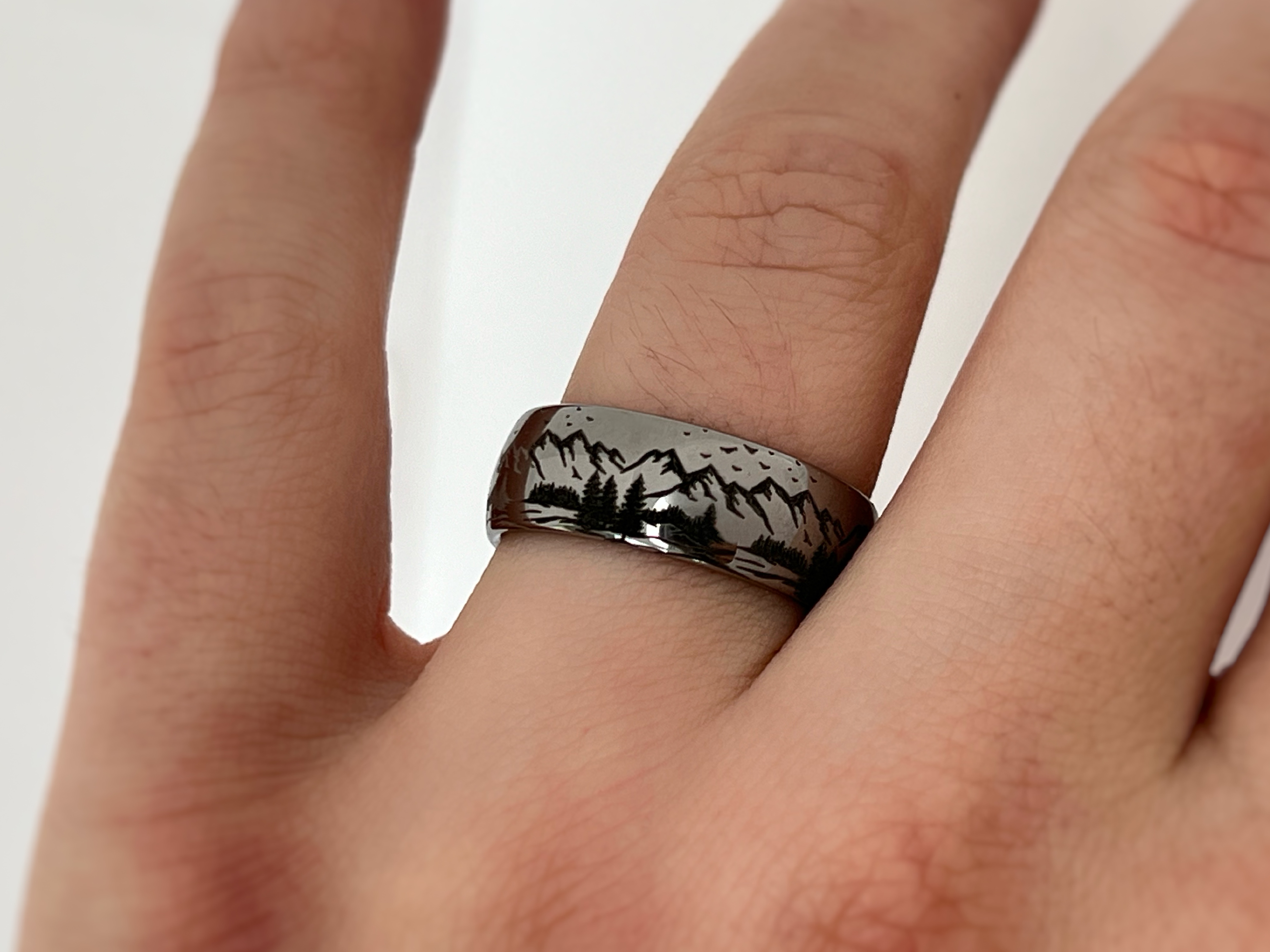 Silver tungsten ring with an engraved mountain range design, worn on a finger, showcasing the detailed engraving.