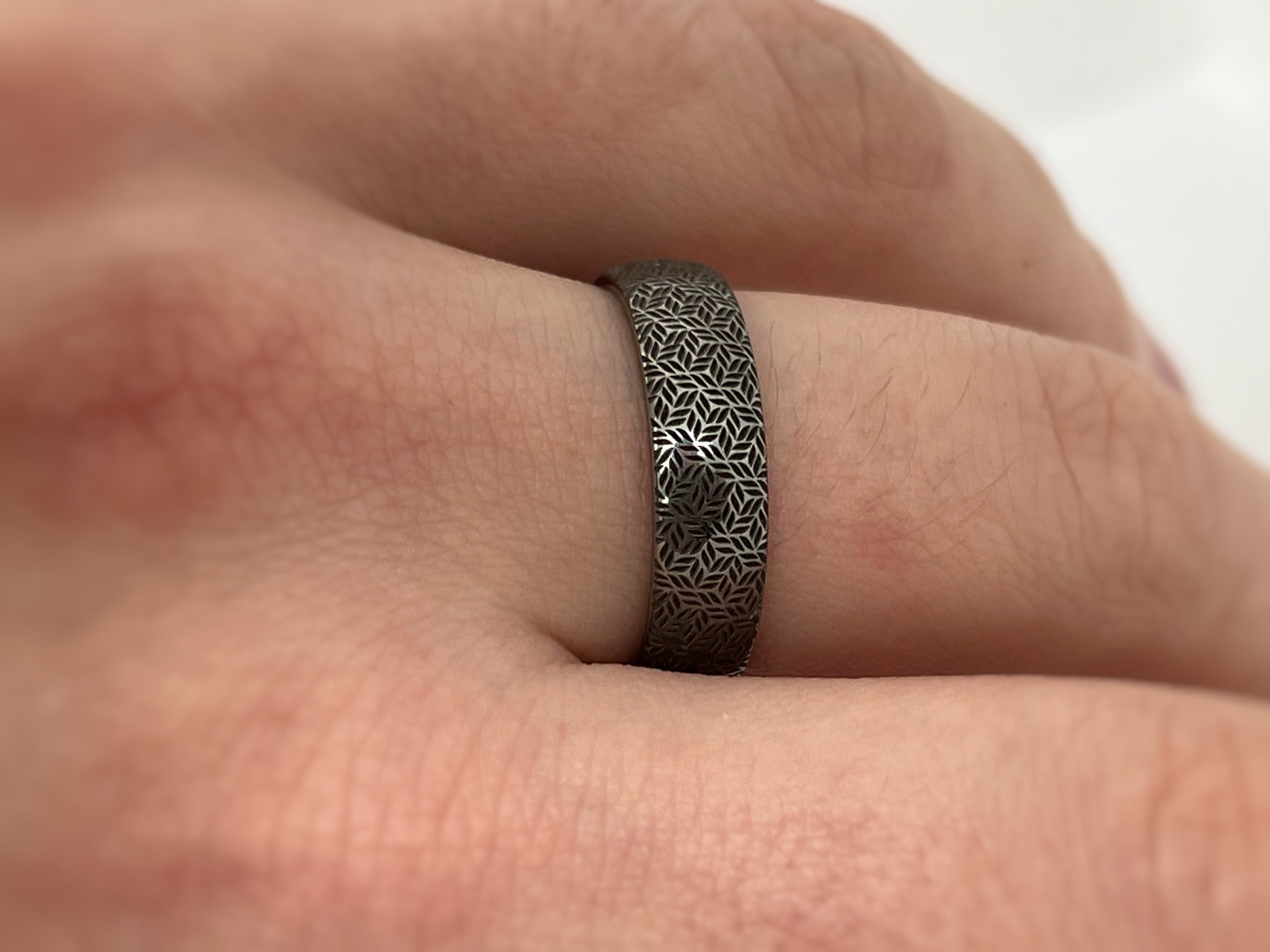 Silver tungsten ring with an intricate leaf pattern, worn on a finger.