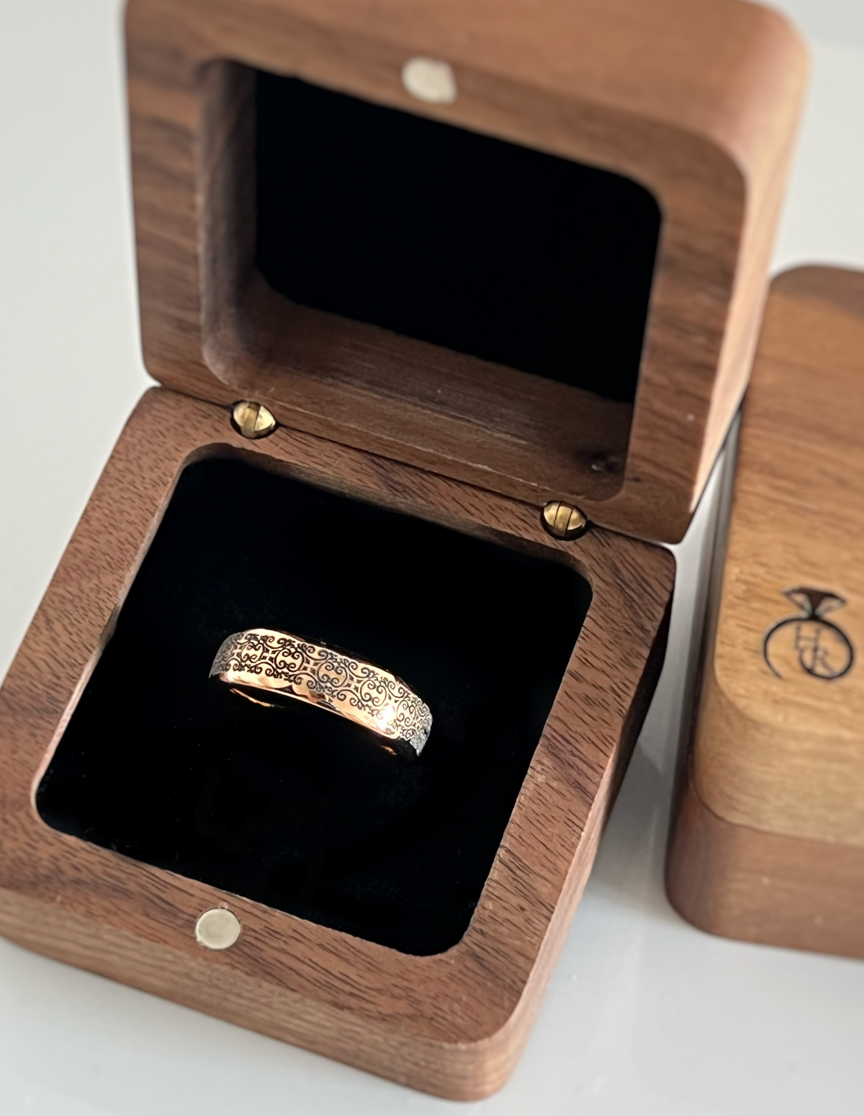 Rose gold tungsten ring with an intricate black swirl design, elegantly displayed in a wooden ring box