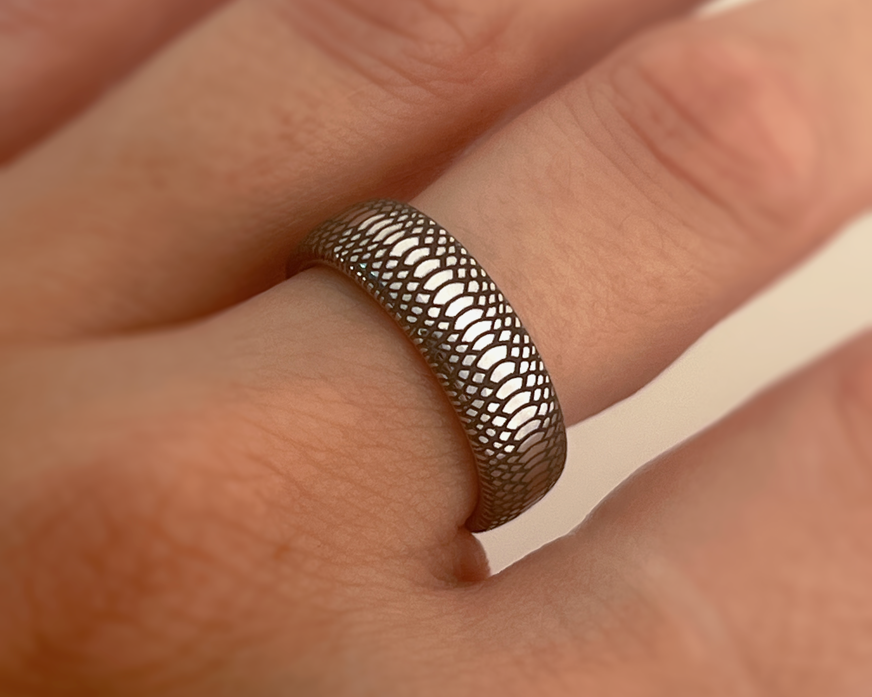 Close-up of a hand wearing a textured silver ring on a neutral background
