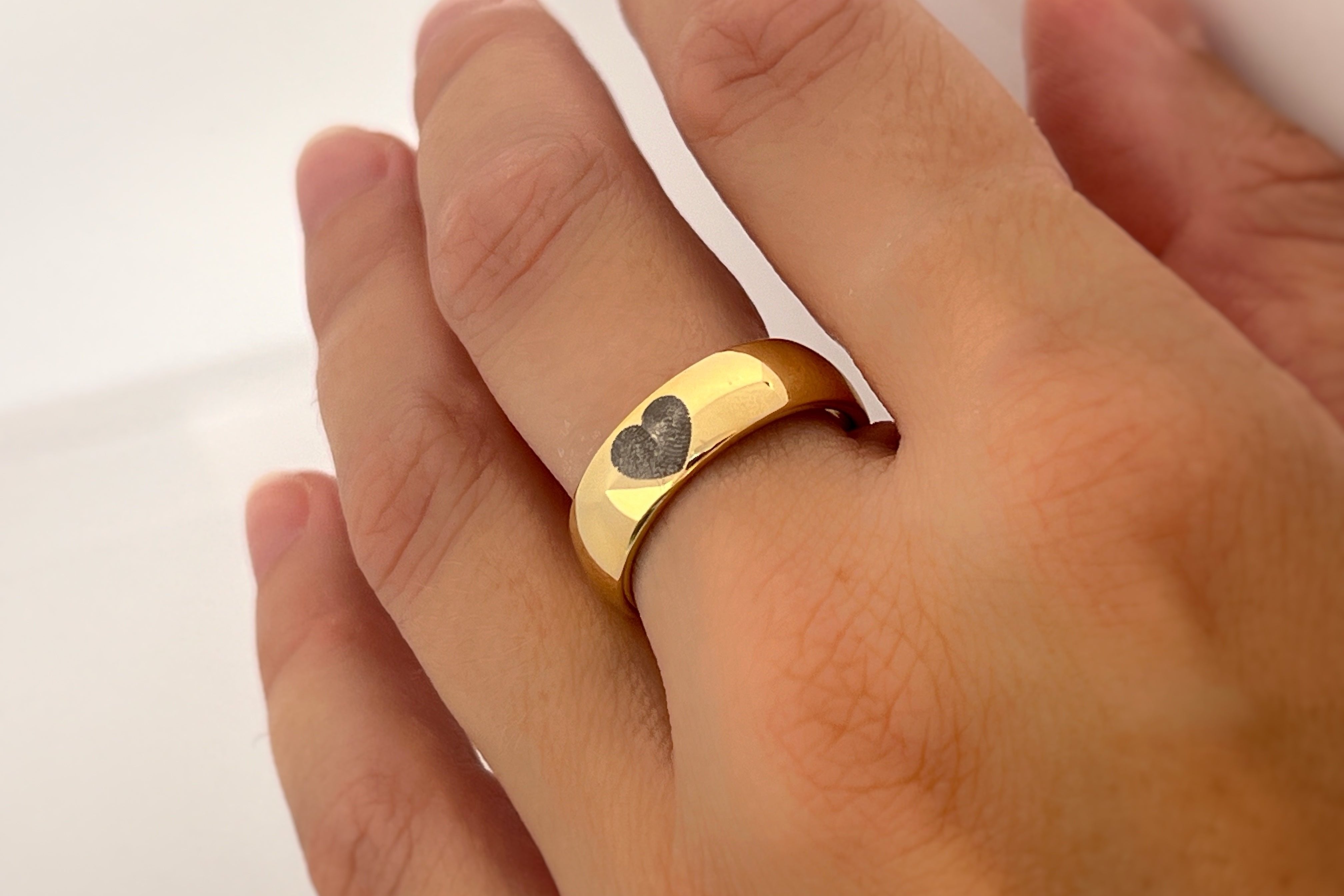 Yellow gold tungsten ring with engraved fingerprint in the shape of heart worn on finger.