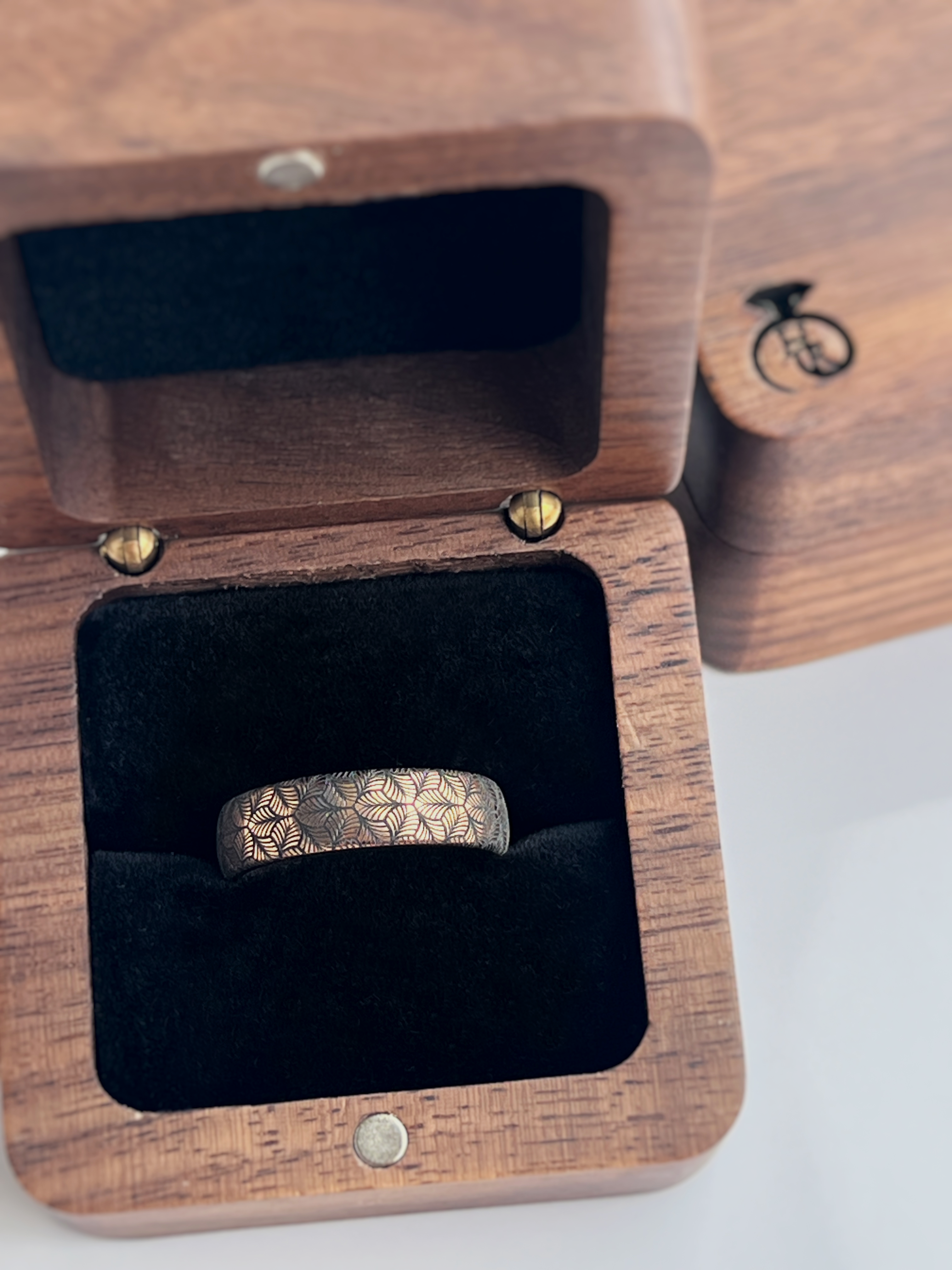 Rose gold tungsten ring with an intricate, black-engraved petal-like pattern, inside wooden box offering a delicate and refined look, perfect for weddings, special occasions, or everyday wear.