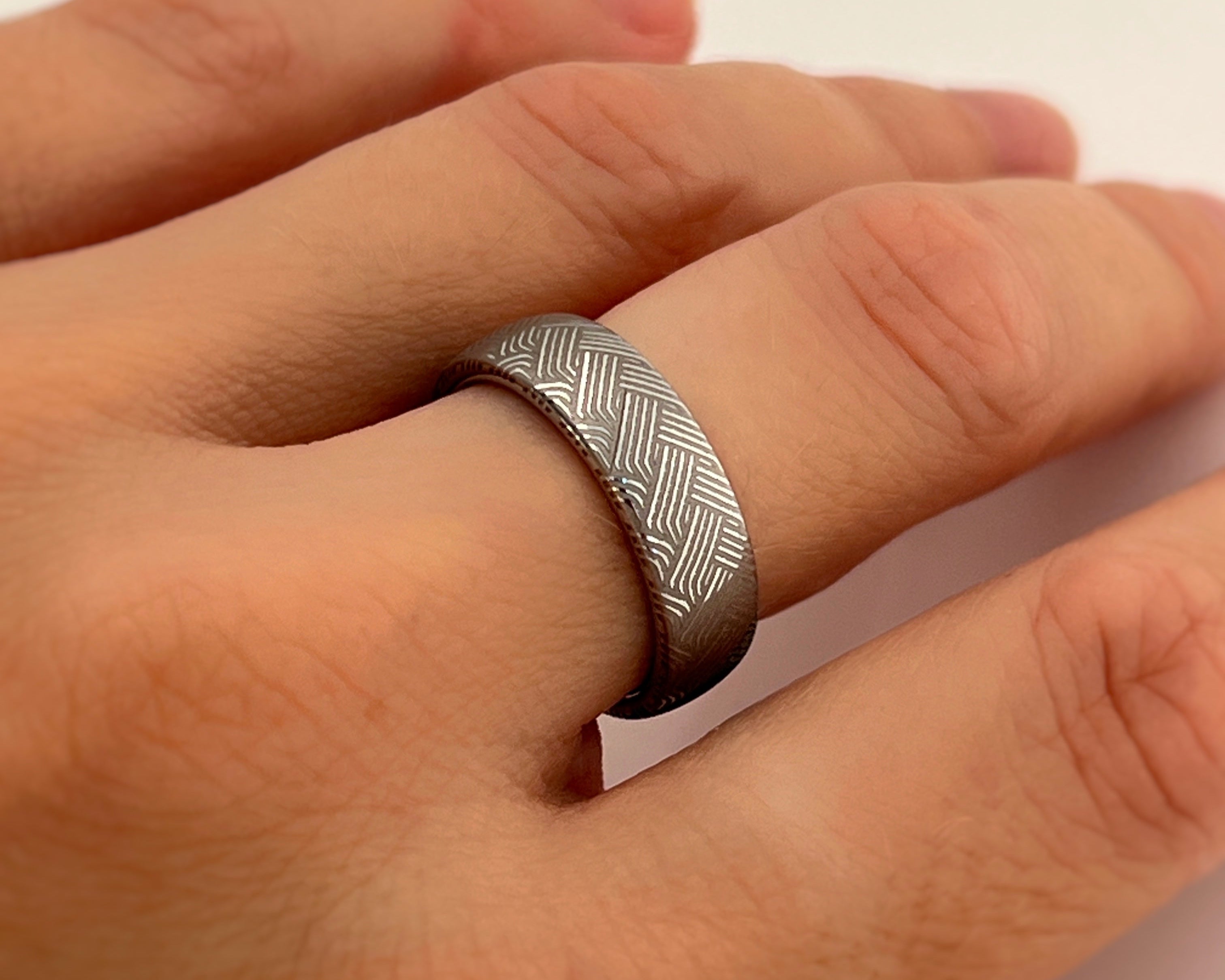 Hand wearing a silver ring with a textured pattern on a light background