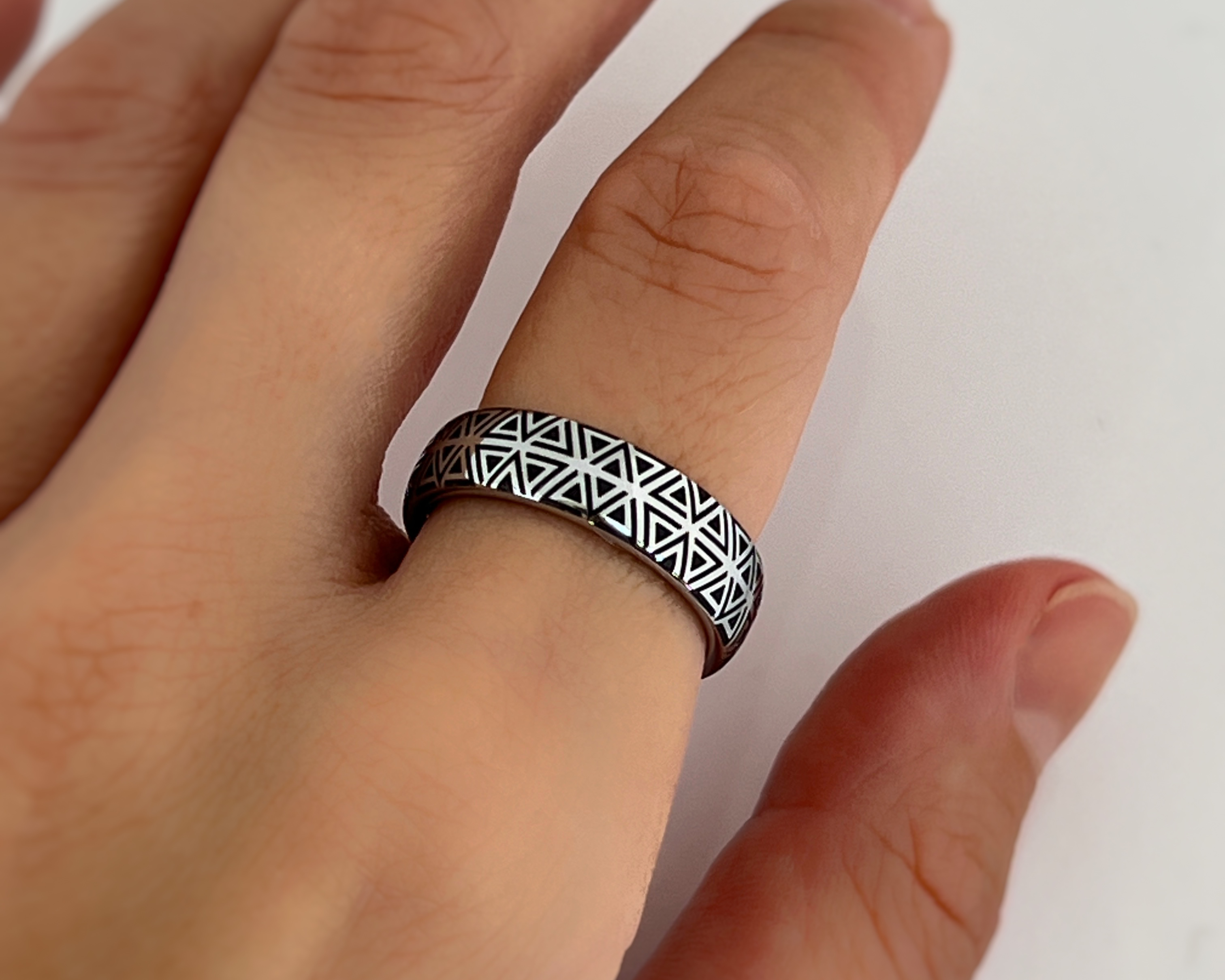 Hand wearing a black and silver geometric patterned ring on a white background