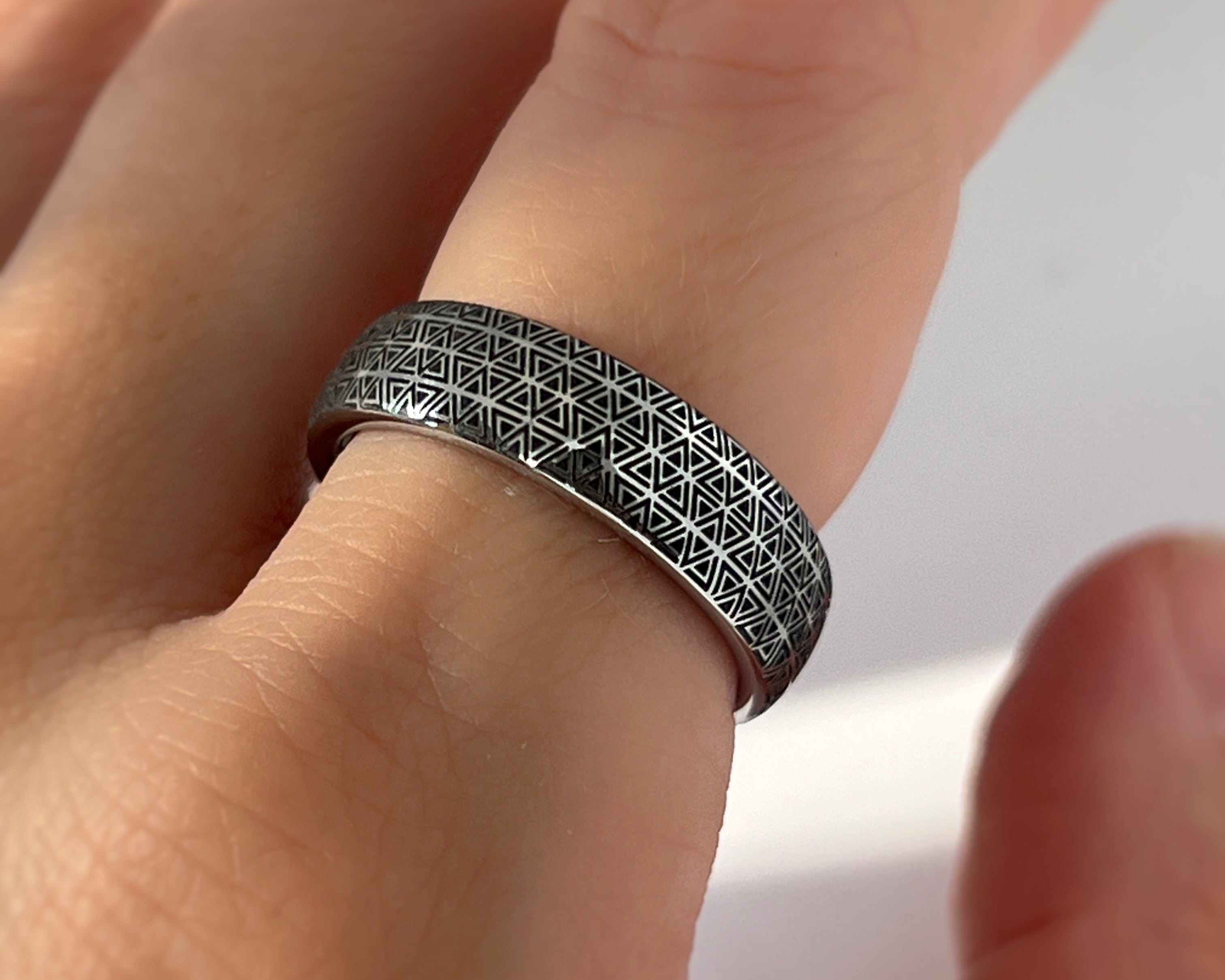 Hand wearing a silver ring with geometric pattern on a light background
