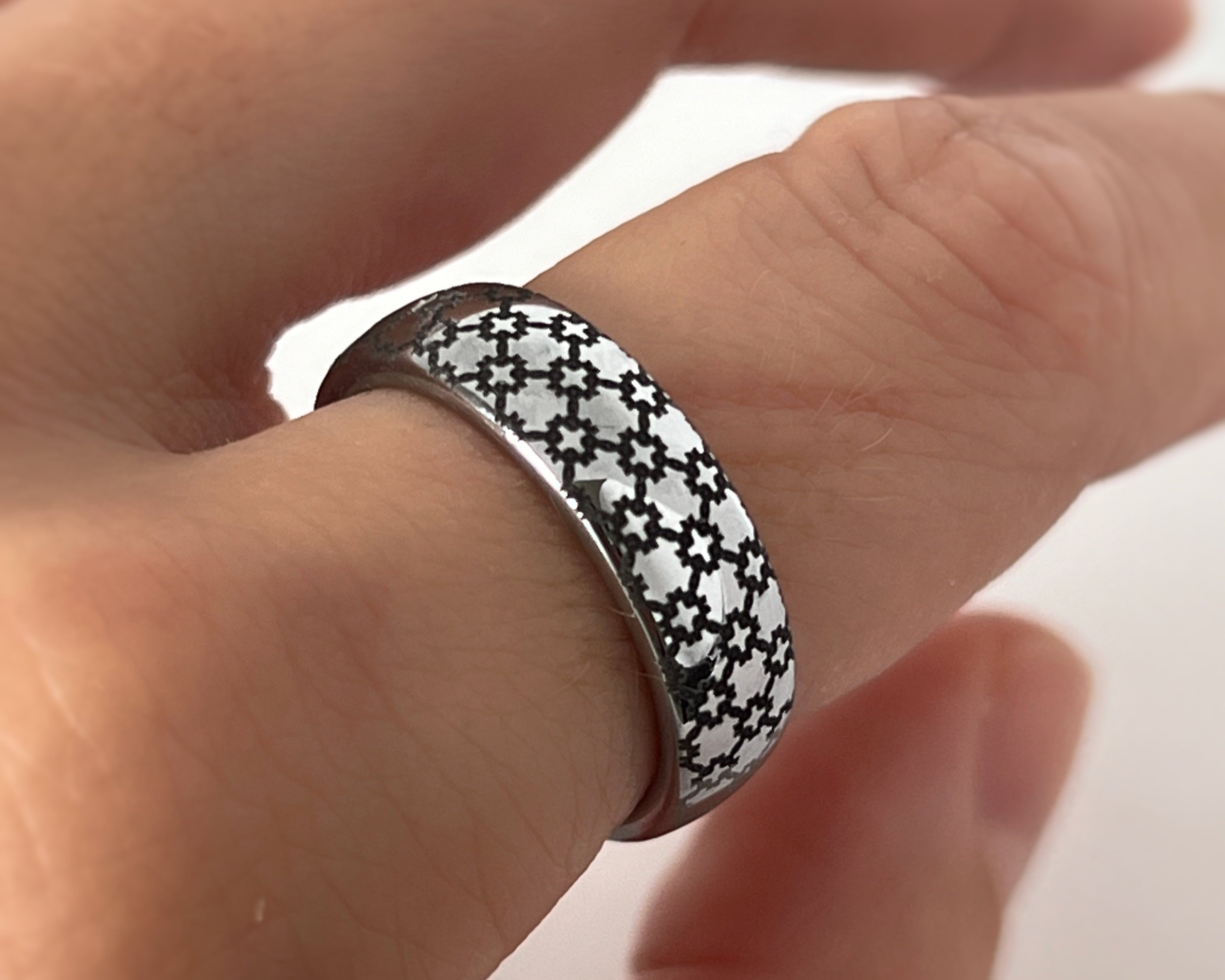 Hand wearing a silver ring with black geometric pattern on a blurred background