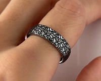 Close-up of a silver tungsten ring worn on hand, featuring intricate black botanical leaf engraving. Elegant nature inspired wedding band with polished finish.