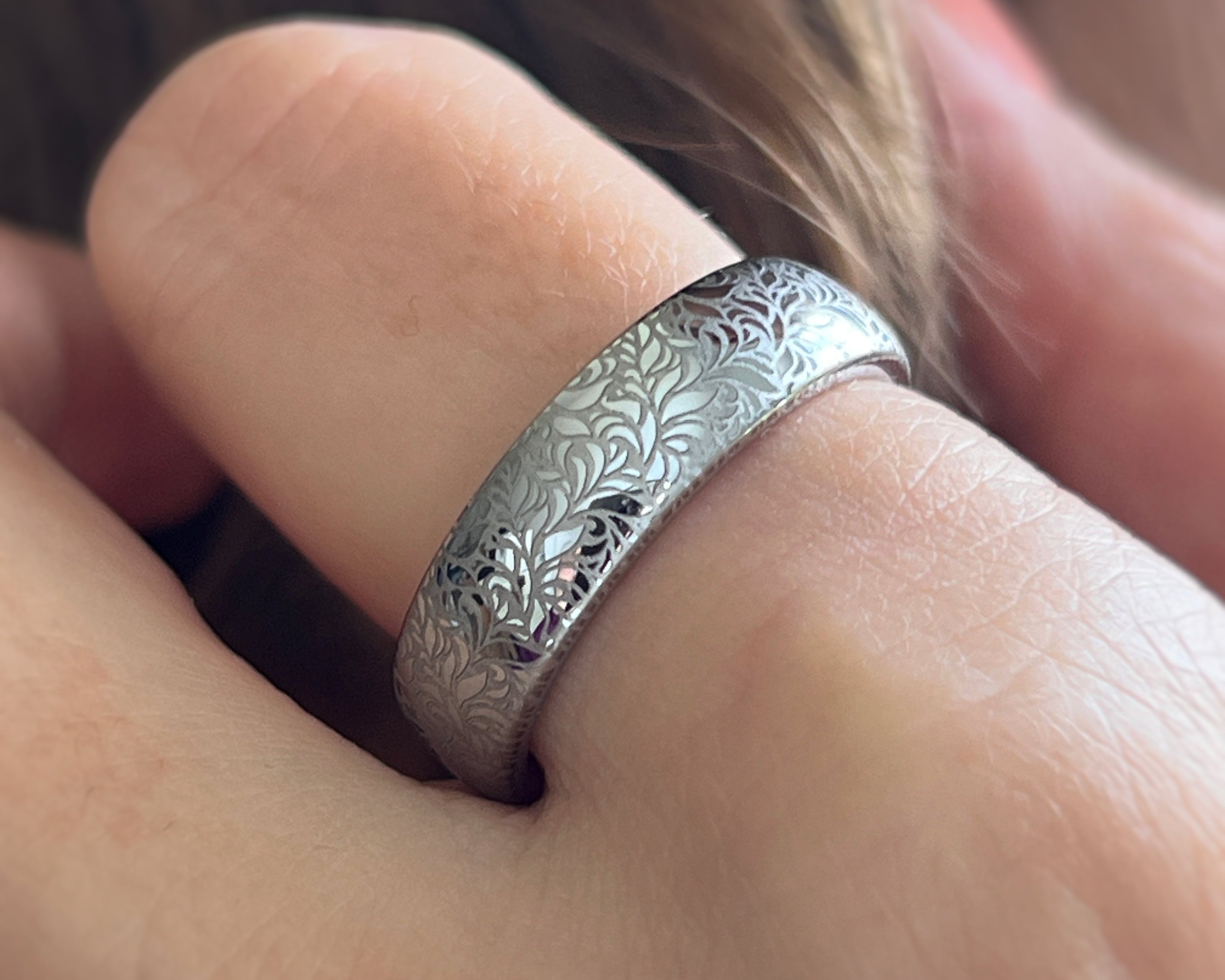 Elegant white gold tungsten ring worn on hand with intricate silver floral engraving, featuring a polished shiny finish and delicate patterns. Durable and stylish, this engraved tungsten wedding or engagement band for her or him