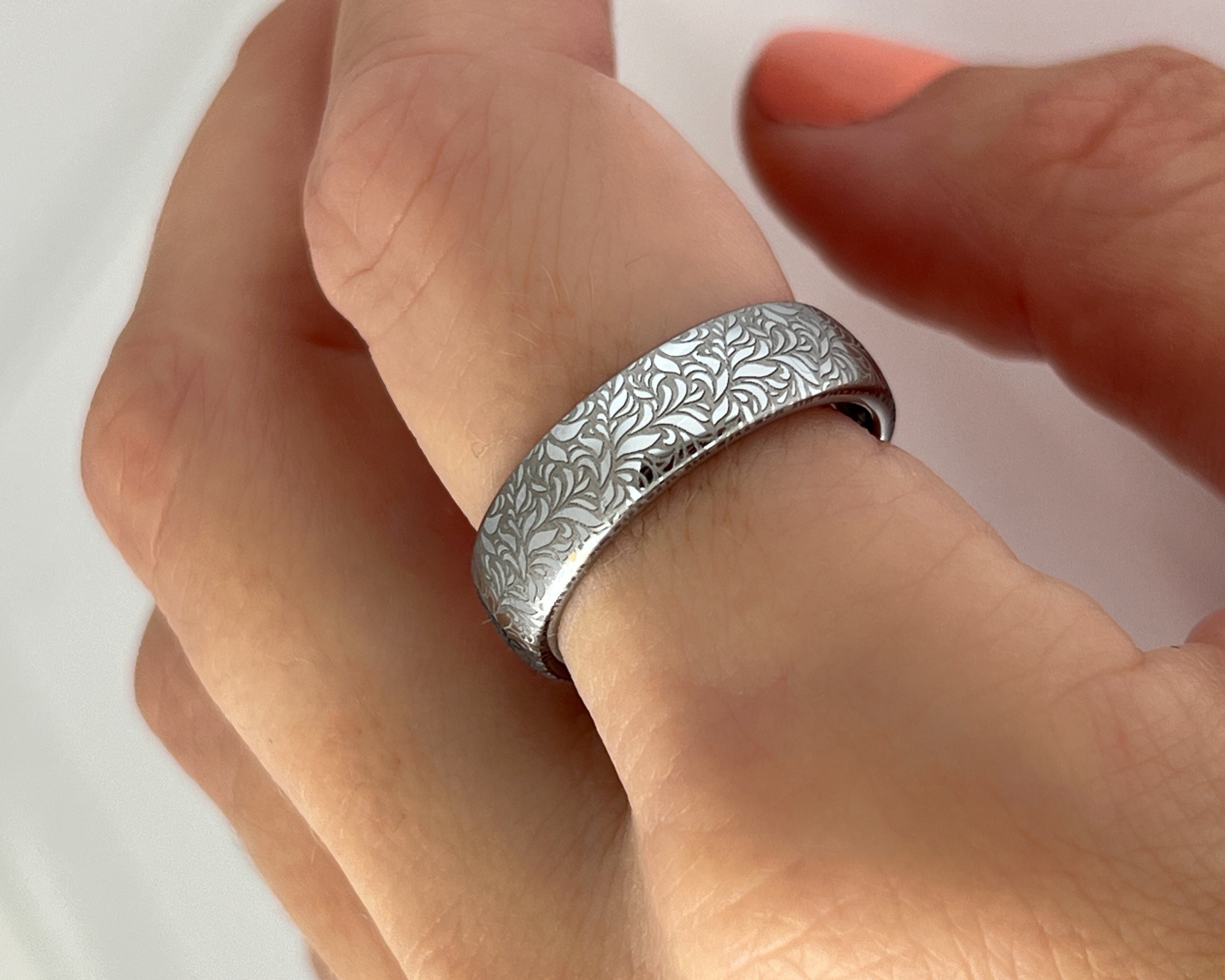 Elegant white gold tungsten ring worn on hand with intricate silver floral engraving, featuring a polished shiny finish and delicate patterns. Durable and stylish, this engraved tungsten wedding or engagement band for her or him