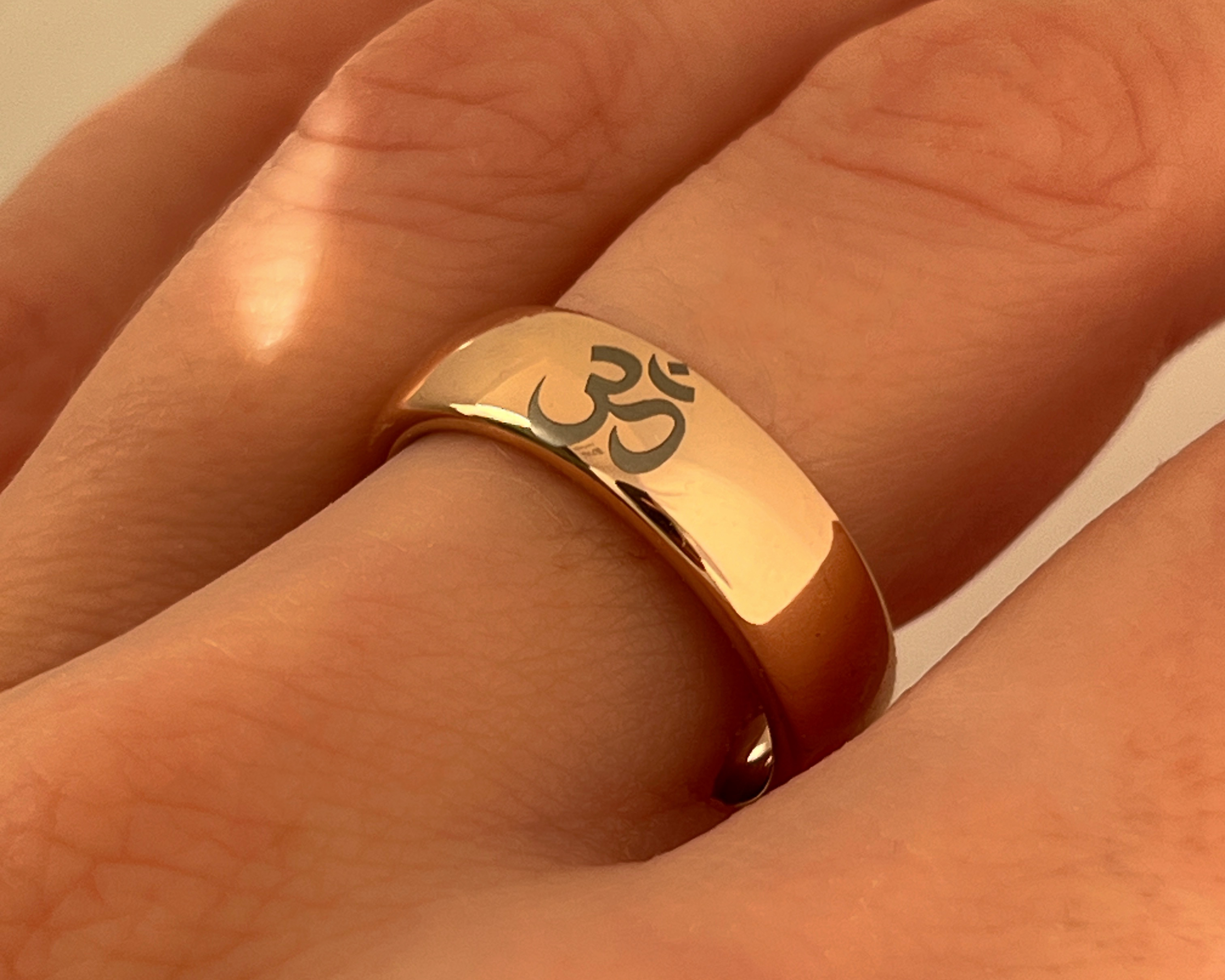 Gold ring with a symbol on a person's finger against a neutral background