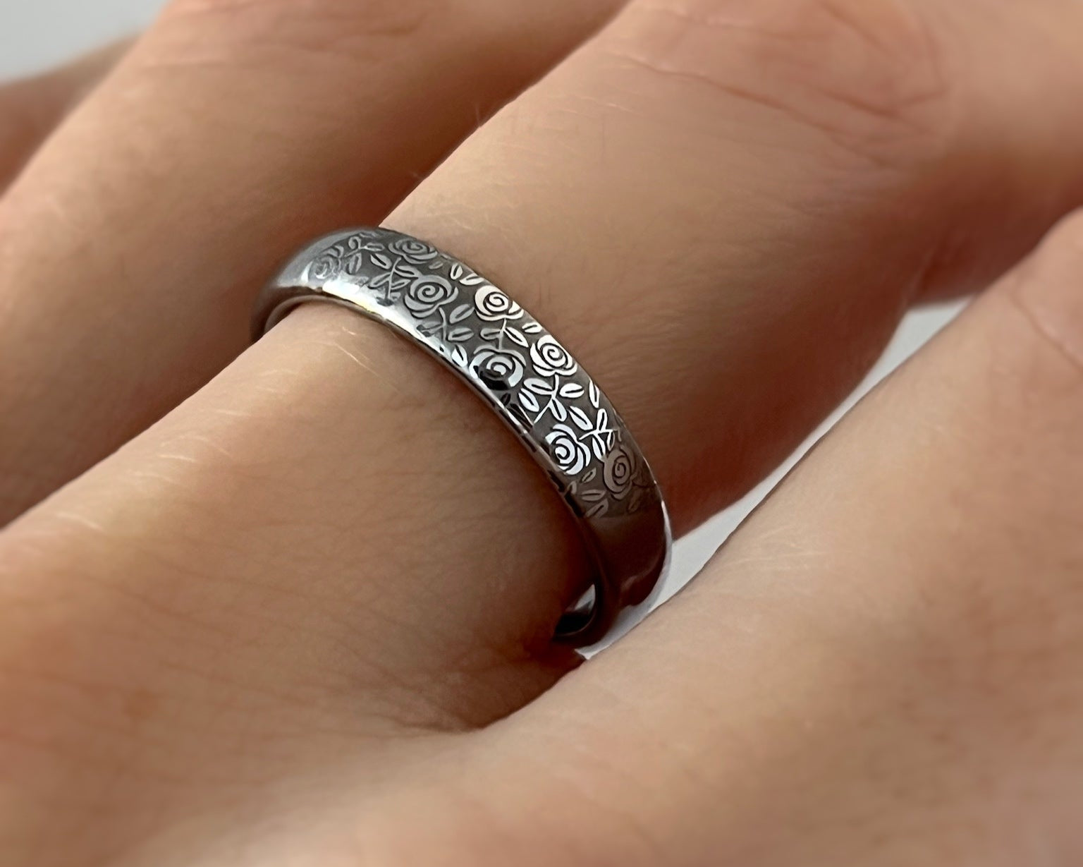 Silver ring with intricate floral design on a person's finger against a white background