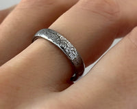 Silver ring with intricate floral design on a person's finger against a white background