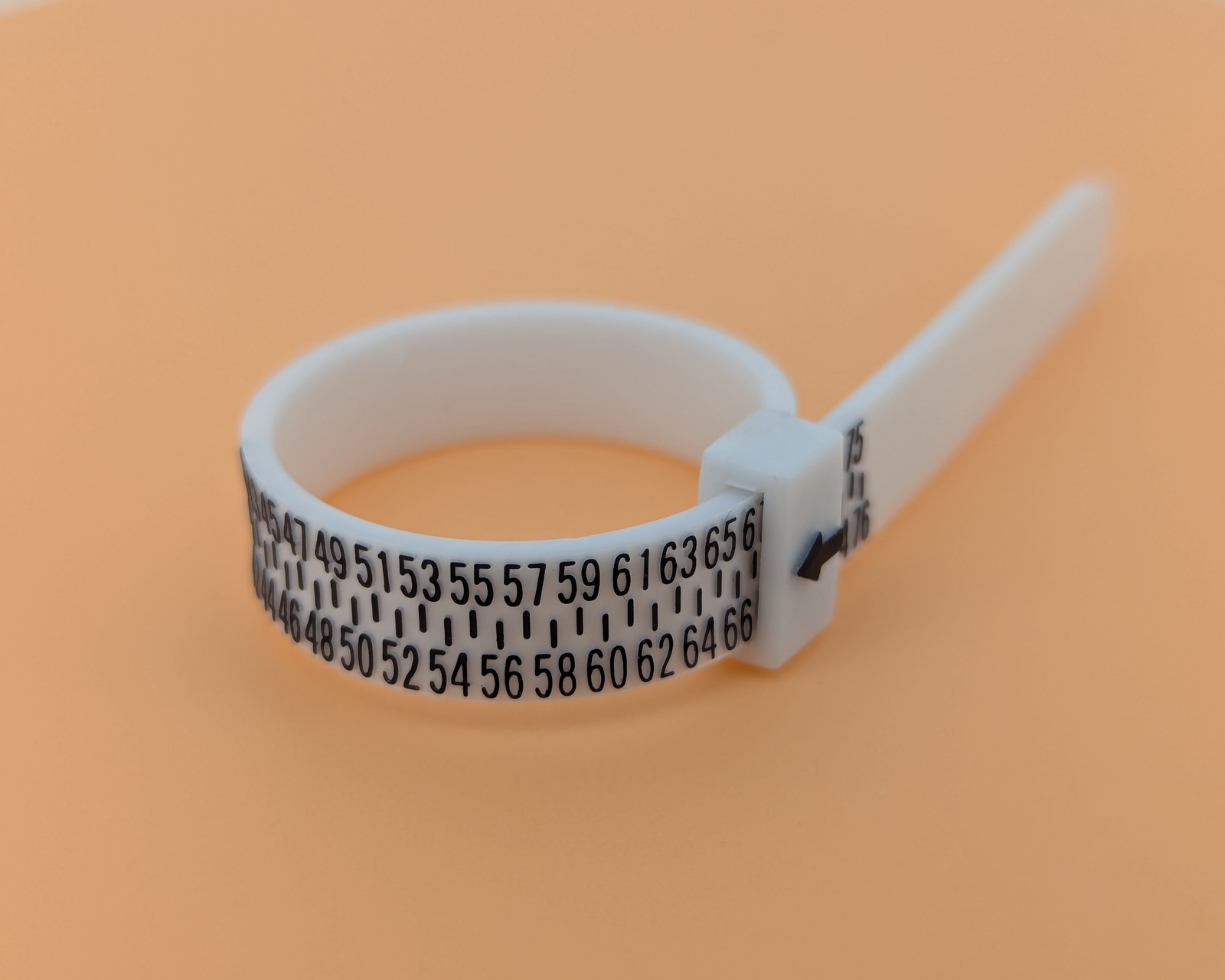 A white plastic ring sizer with black numbers and markings, placed on an orange background.