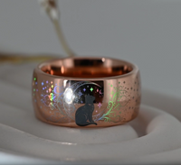 Anillo Mystic Whiskers de color oro rosa con un gato negro, estrellas y reflejos de arcoíris cambiantes sobre un soporte claro.
