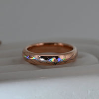 Rose-gold Heartline tungsten ring with holographic lines forming a heart, resting on a pale display surface.