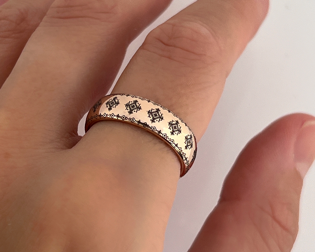 Close-up of a hand wearing a rose gold tungsten ring with engraved traditional ornamental pattern, photographed against a white background.