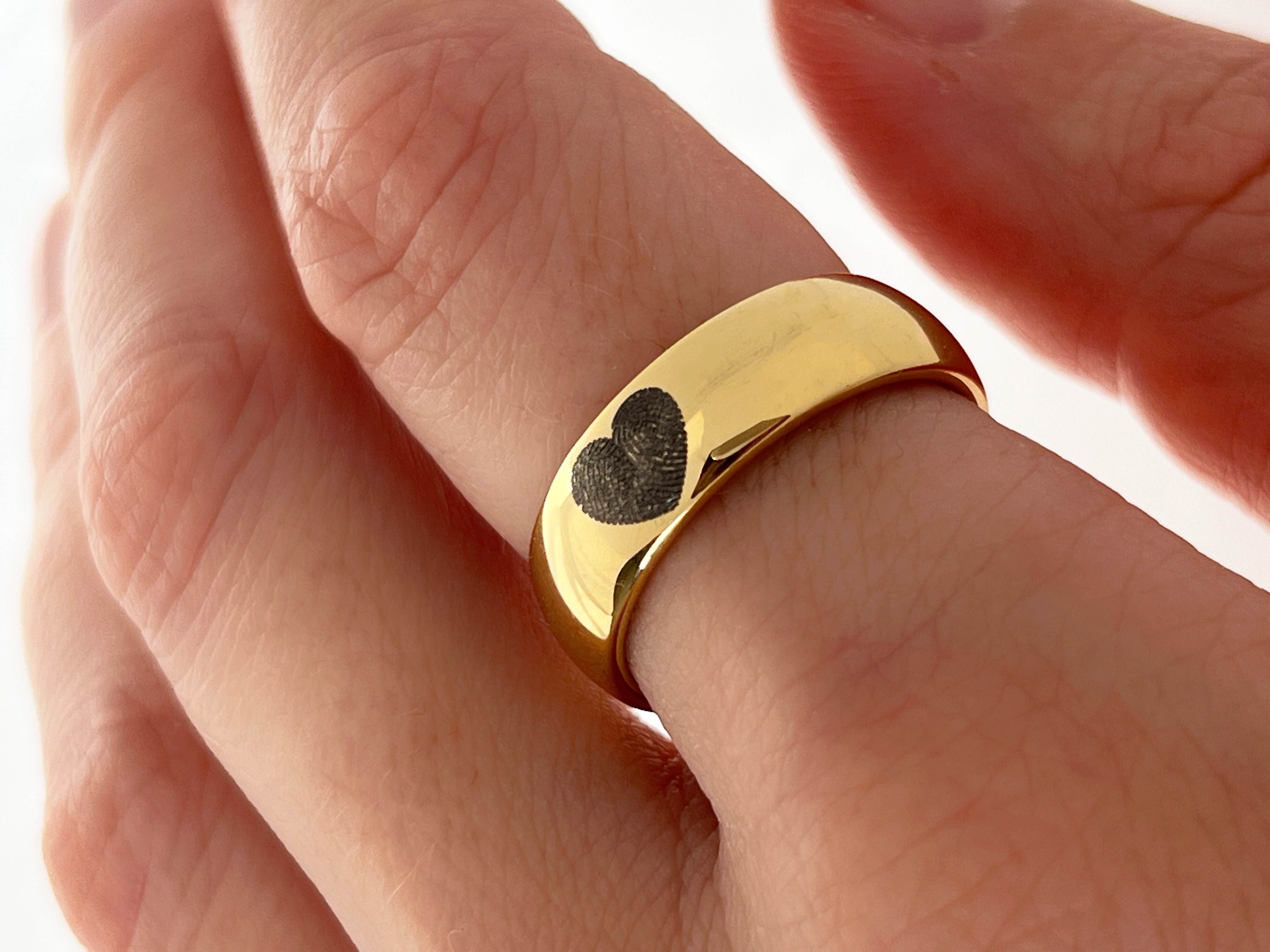 Yellow gold tungsten ring with engraved fingerprint in the shape of heart worn on finger.