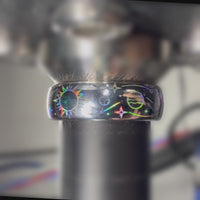 Close-up video of a Celestial Orbit ring on a metal holder, showing rainbow reflections across planets, stars and orbit lines.