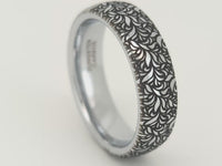 Video of a silver tungsten ring rotating on a light background, showcasing an intricate black botanical leaf engraving and polished finish. Elegant nature inspired wedding band with detailed floral design.