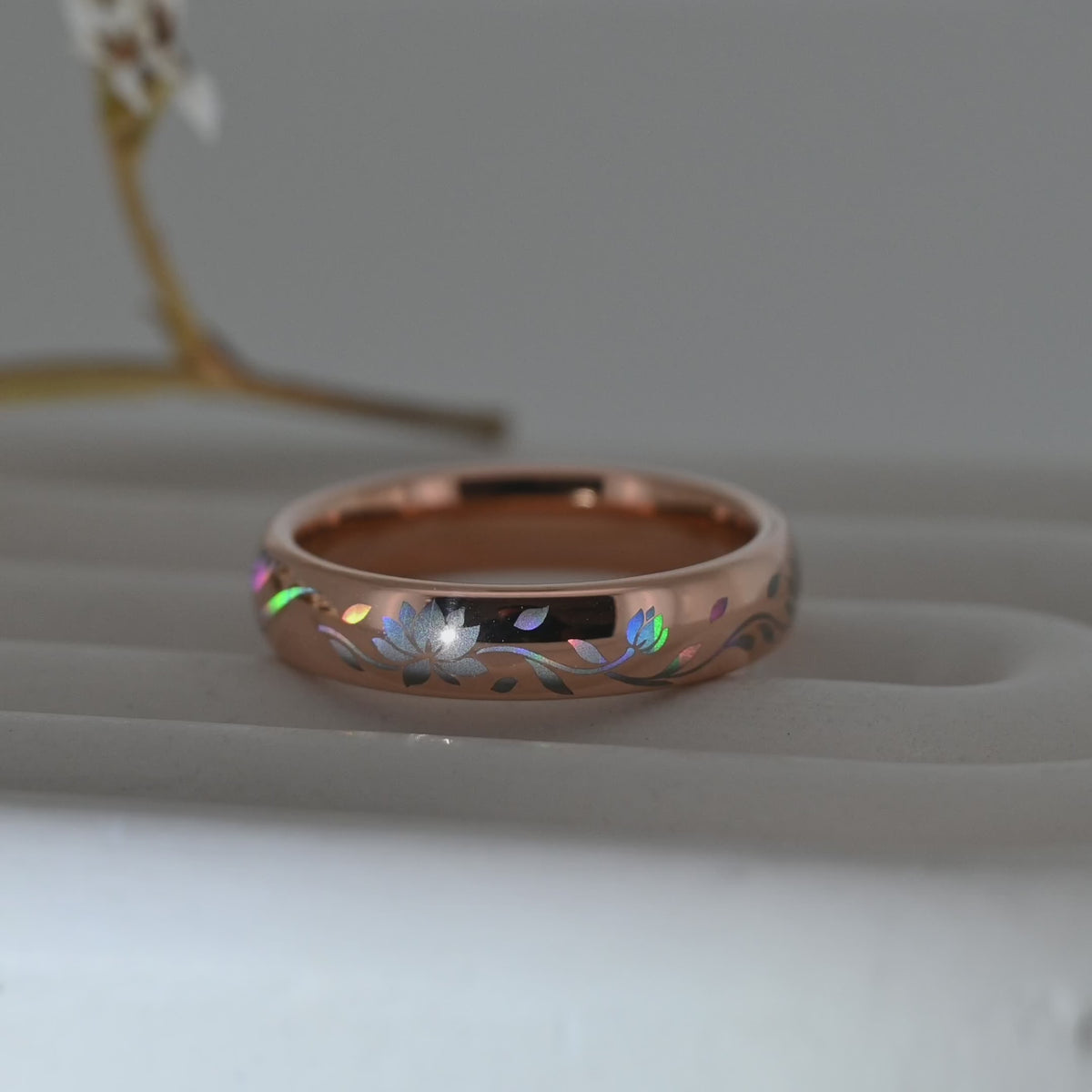 Video of a rose-gold Lotos Glow tungsten ring on a pale display surface, showing a holographic lotus flower and flowing leaves.
