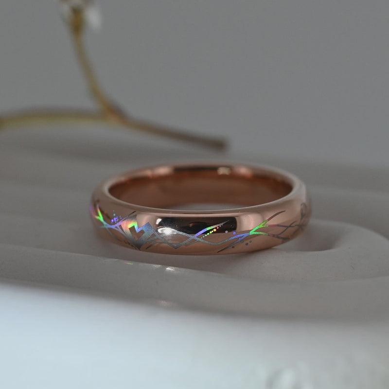 Video of a rose-gold Heartline tungsten ring on a pale display surface, showing holographic lines forming a heart motif.