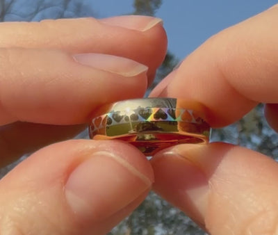 Close-up video of the HoloHearts ring held between fingers in sunlight, revealing shimmering holographic heart details on a polished gold band. Romantic statement ring with reflective sparkle effect.
