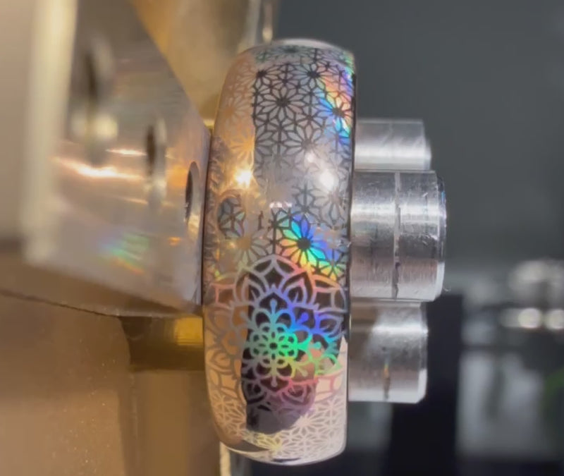 Close-up video of the Boho Holo Mandala tungsten ring during the engraving process, showing a mandala-inspired pattern with holographic rainbow reflections under the light.