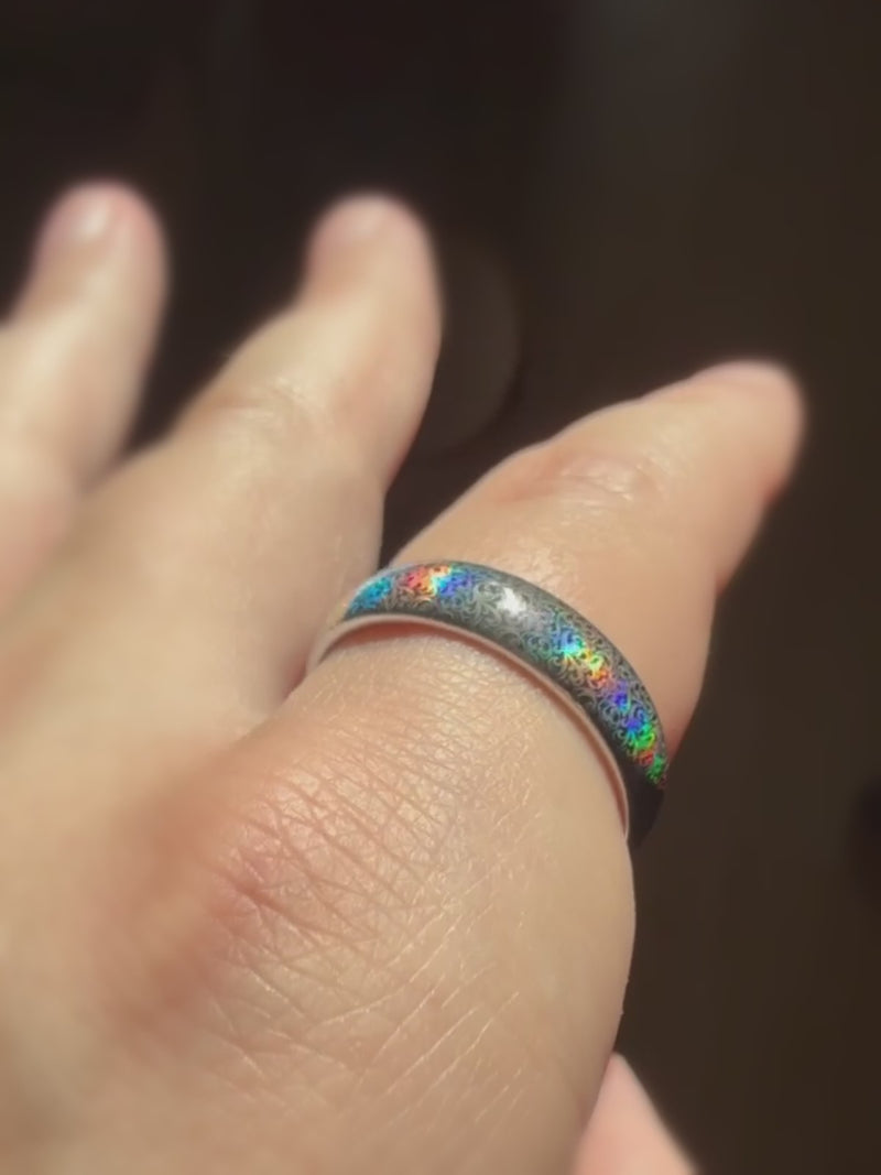 Baroque Radiance holographic tungsten ring worn on a finger in warm light.