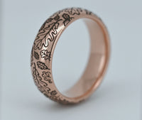ideo of a rose gold tungsten ring with engraved oak leaf pattern rotating on a clean white background. Nature inspired wedding band with polished finish and detailed botanical design.