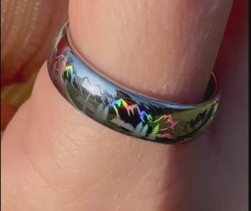Close-up video of the Radiant Mountains holographic tungsten ring, showing mountain, forest and wildlife silhouettes shifting through rainbow colors in the light.