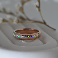 Video of a rose-gold Sakura Glow tungsten ring on a pale display surface, showing holographic sakura blossoms and flowing leaves.
