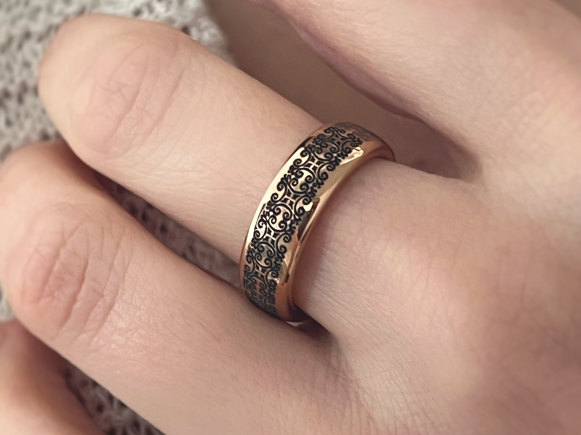 Rose gold tungsten ring with an antique black swirl pattern, shown on a person's finger against a textured fabric background.